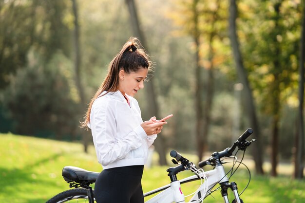 Joven mujer caucásica descansando en un parque, utiliza un teléfono móvil.