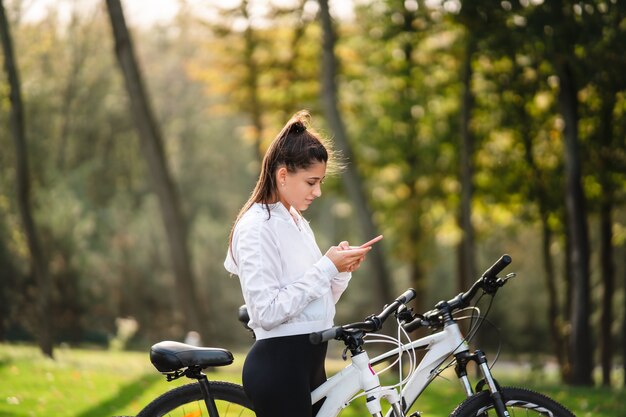 Joven mujer caucásica descansando en un parque, utiliza un teléfono móvil.