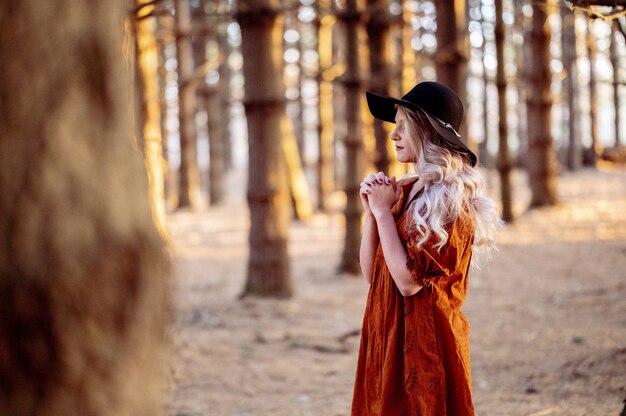 Joven mujer caucásica en un elegante sombrero negro rezando en el bosque escénico, humor otoñal