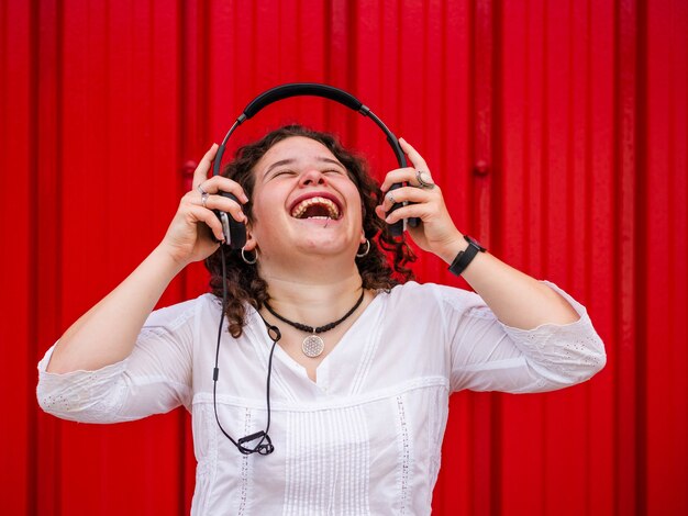 Joven mujer caucásica escuchando felizmente meditando con auriculares cerca de una pared roja