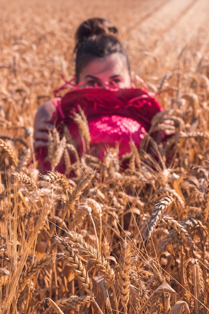 Joven mujer caucásica en un hermoso vestido rojo disfrutando del clima soleado en un campo de trigo