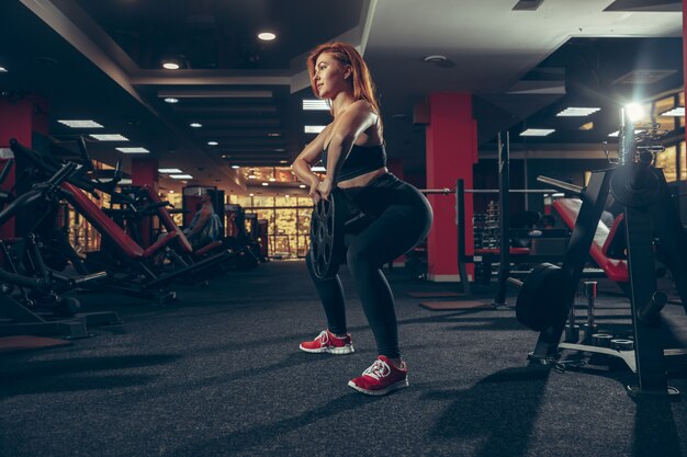 Joven mujer caucásica muscular practicando en el gimnasio con equipo. Bienestar, estilo de vida saludable, culturismo.