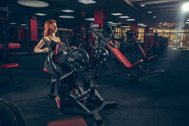 Joven mujer caucásica muscular practicando en el gimnasio con equipo. Bienestar, estilo de vida saludable, culturismo.