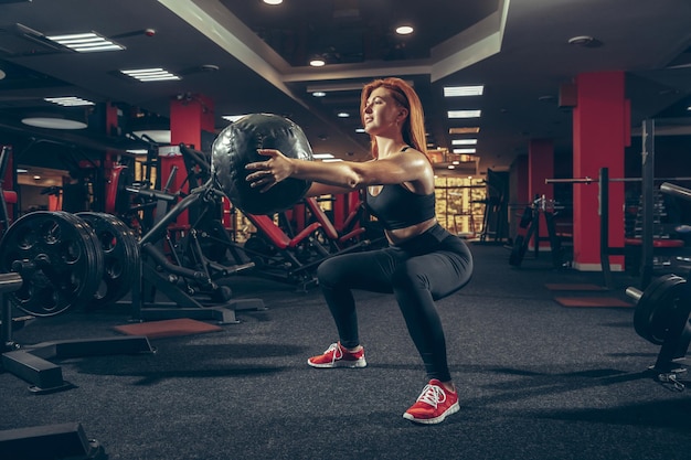 Joven mujer caucásica muscular practicando en el gimnasio con equipo.