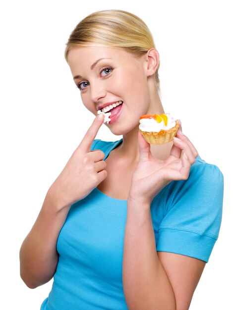 Joven mujer caucásica con pastel dulce en mano y crema blanca en su dedo