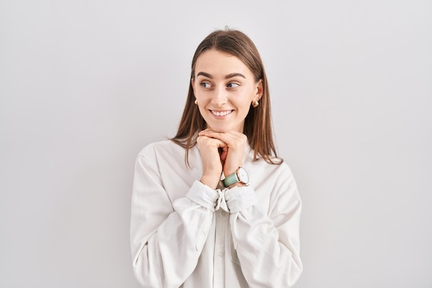 Foto gratuita joven mujer caucásica de pie sobre un fondo aislado riéndose nerviosa y emocionada con las manos en la barbilla mirando hacia un lado