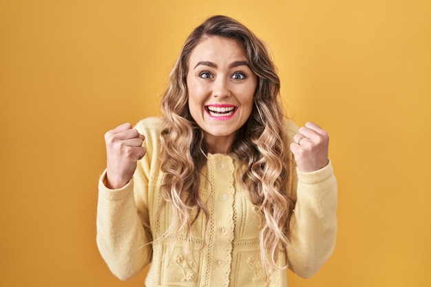 Joven mujer caucásica de pie sobre fondo amarillo celebrando sorprendida y asombrada por el éxito con los brazos levantados y los ojos abiertos. concepto de ganador.