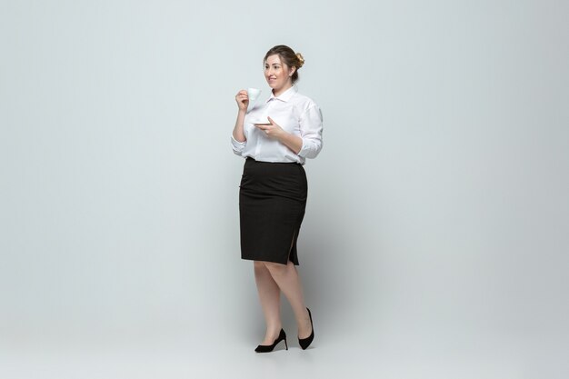 Joven mujer caucásica en traje de oficina en pared gris