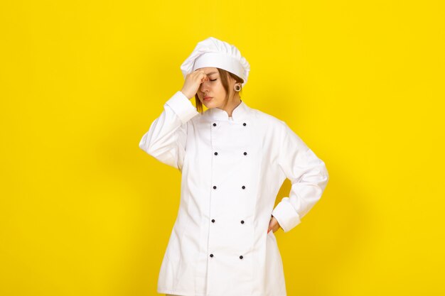 Joven mujer cocinando en traje de cocinero blanco y gorra blanca cansada de tener un fuerte dolor de cabeza