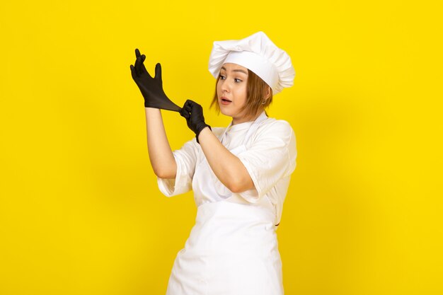 Joven mujer cocinando en traje de cocinero blanco y gorra blanca con guantes negros