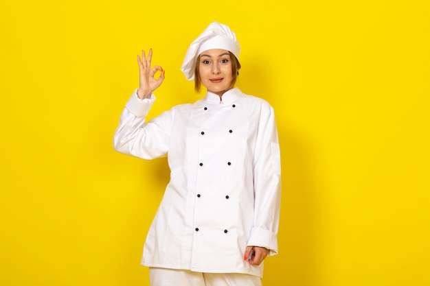 Joven mujer cocinando en traje de cocinero blanco y gorra blanca sonriendo bien signo