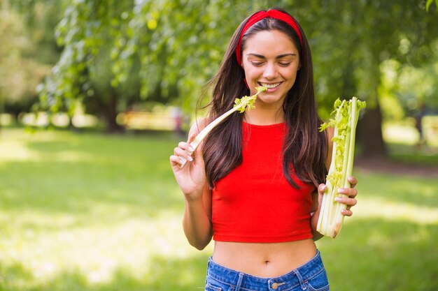 Joven mujer comiendo apio fresco en el parque