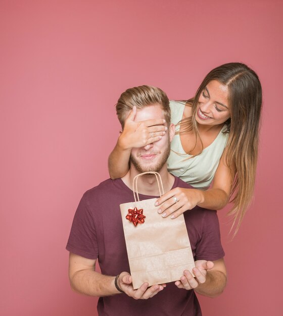 Joven mujer cubriendo los ojos de su novio mientras le da un regalo