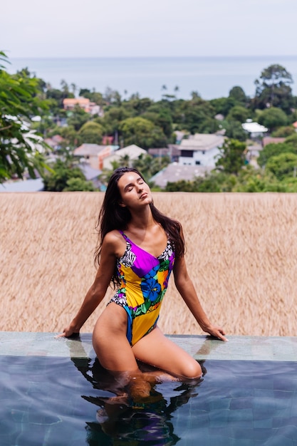 Foto gratuita joven mujer delgada feliz bastante positiva en traje de baño colorido en la villa de lujo increíble hotel disfrutando de un hermoso día de vacaciones en tailandia