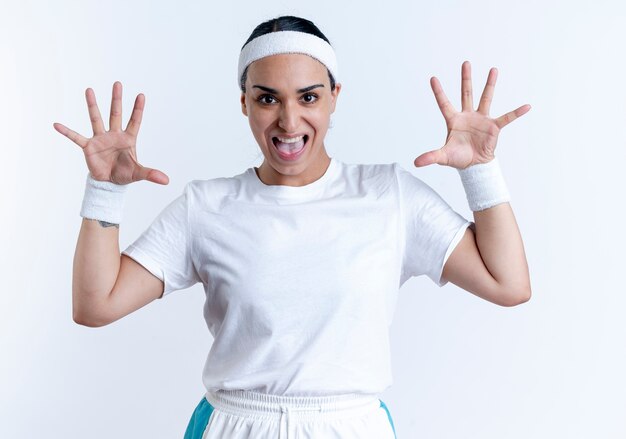 Foto gratuita joven mujer deportiva caucásica alegre vistiendo diadema y muñequeras se encuentra con las manos levantadas