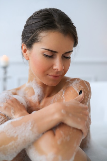 Joven mujer desnuda tomando un relajante baño espumoso