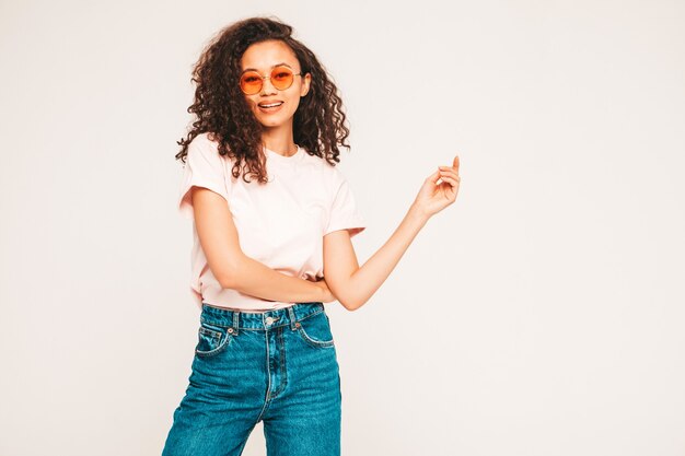 Joven mujer despreocupada posando en la pared gris en estudio con gafas de sol