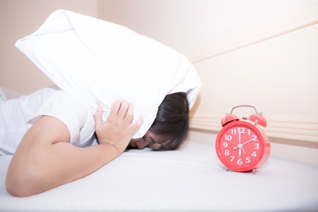 Joven mujer dormida y despertador en el dormitorio en casa