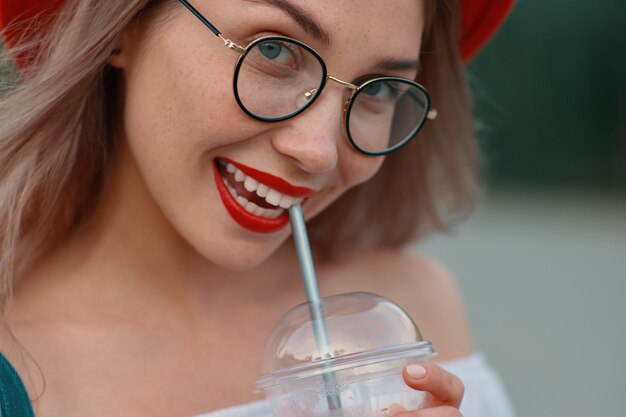 Una joven mujer elegante con una bebida refrescante mientras sonríe