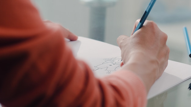 Joven mujer embarazada asiática dibujo bebé en el vientre y la familia en el cuaderno. Mamá se siente feliz sonriendo positiva y pacífica mientras cuida al niño en la mesa en la sala de estar en casa.