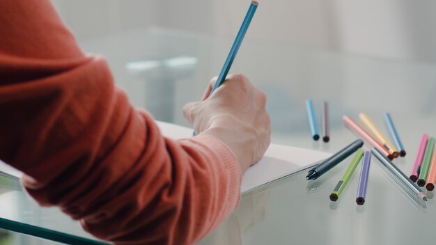 Joven mujer embarazada asiática dibujo bebé en el vientre y la familia en el cuaderno. Mamá se siente feliz sonriendo positiva y pacífica mientras cuida al niño en la mesa en la sala de estar en casa.