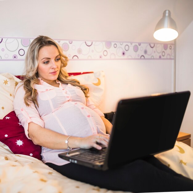 Joven mujer embarazada usando la computadora portátil