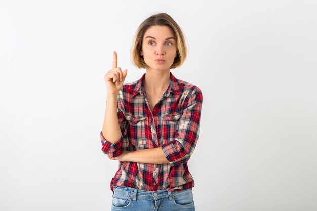 Joven mujer emocional bastante divertida en camisa a cuadros posando aislado en la pared blanca del estudio, mostrando gesto