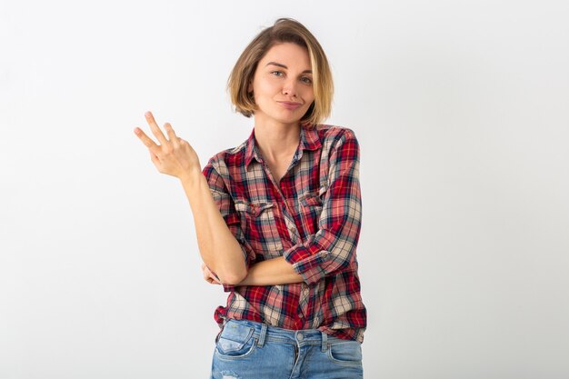 Joven mujer emocional bastante divertida en camisa a cuadros posando aislado en la pared blanca del estudio, mostrando gesto