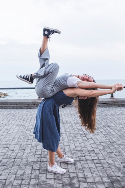 Joven mujer de equilibrio amigo en la espalda de pie cerca del mar