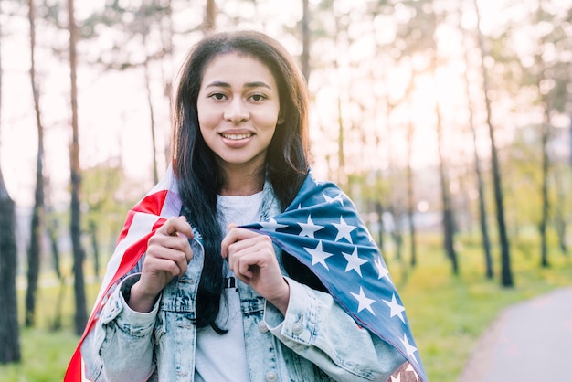 Joven mujer étnica envuelta en bandera americana