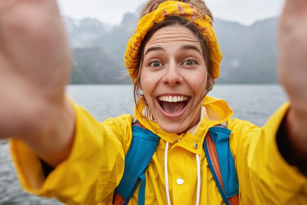 Joven mujer exagerada en anorak amarillo y diadema, estira las manos con dispositivo irreconocible