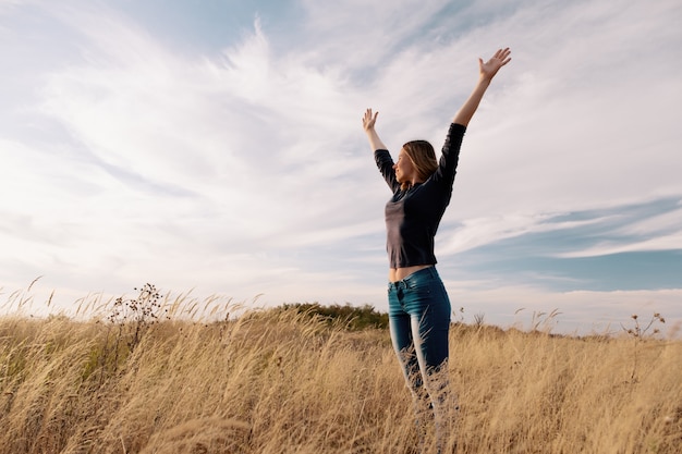 Joven mujer feliz en un campo de oro en puesta de sol.