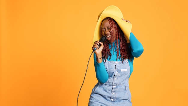 Foto gratuita joven mujer feliz cantando en el micrófono, haciendo karaoke frente a la cámara. cantante alegre y talentosa que tiene una actuación musical en vivo en el estudio, de pie sobre un fondo naranja.