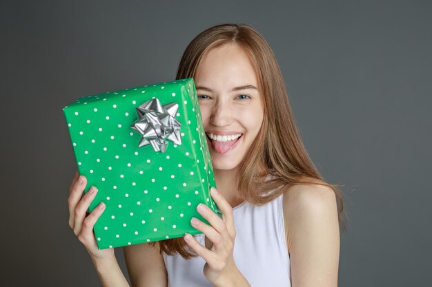 Joven mujer feliz dando caja de regalo a la cámara con una sonrisa emocionada saludando en vacaciones y compartiendo presente