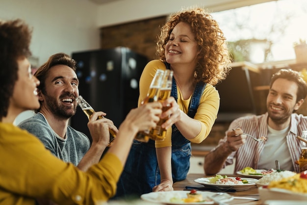 Joven mujer feliz divirtiéndose mientras brinda con sus amigos durante un almuerzo en la mesa del comedor