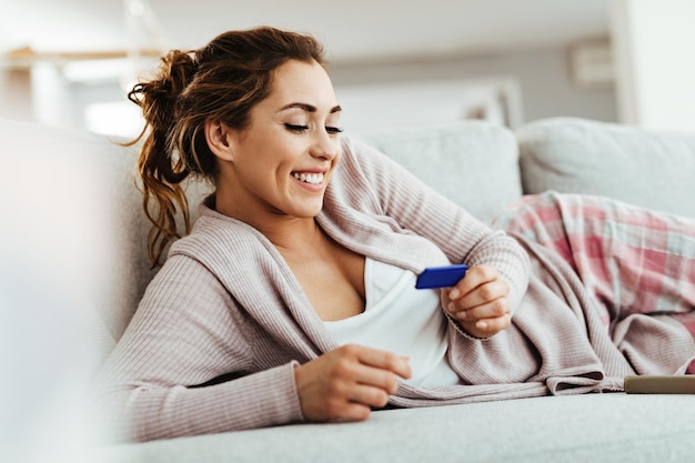 Joven mujer feliz esperando el resultado de la prueba de embarazo mientras se relaja en casa