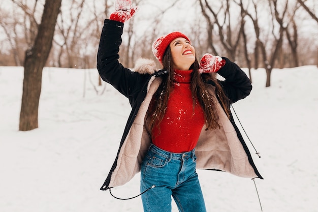 Joven mujer feliz muy sonriente en guantes rojos y gorro de punto con abrigo de invierno caminando en el parque en la nieve, ropa de abrigo, divirtiéndose