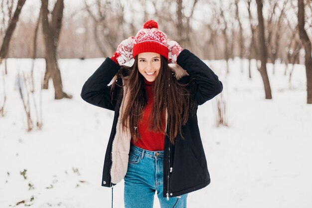 Joven mujer feliz muy sonriente en guantes rojos y gorro de punto con abrigo de invierno, caminando en el parque en la nieve, ropa de abrigo