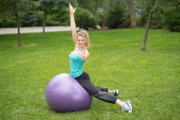 Joven mujer feliz con pelota de fitness, al aire libre