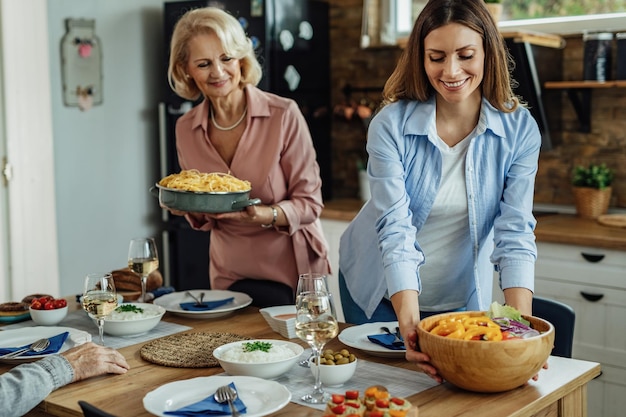 Joven mujer feliz sirviendo ensalada mientras prepara la mesa para el almuerzo.