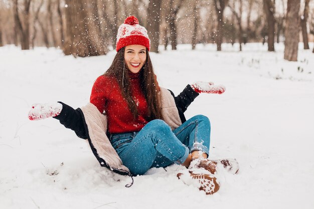Joven mujer feliz sonriente bastante sincera en guantes rojos y gorro de punto con abrigo negro caminando jugando en el parque en la nieve, ropa de abrigo, divirtiéndose