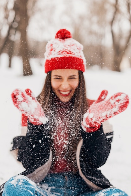 Joven mujer feliz sonriente bastante sincera en guantes rojos y gorro de punto con abrigo negro caminando jugando en el parque en la nieve, ropa de abrigo, divirtiéndose