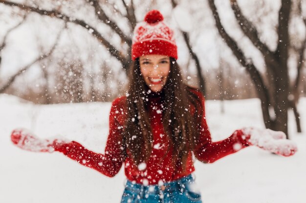 Joven mujer feliz sonriente bastante sincera en guantes rojos y sombrero con suéter de punto caminando jugando en el parque en la nieve, ropa de abrigo, divirtiéndose