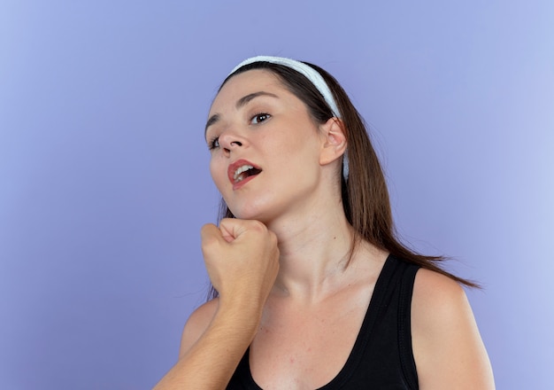 Joven mujer fitness en diadema siendo perforada en su cara sobre la pared azul
