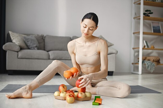 Joven mujer fitness sentada en una alfombra de yoga en casa y sosteniendo manzanas frescas