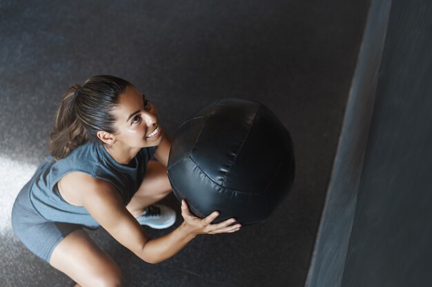 Joven mujer fuerte levanta la bola como realizar ejercicio de sentadillas