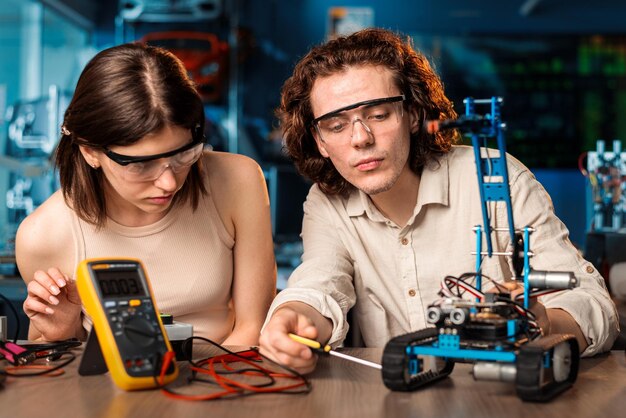 Joven y mujer con gafas protectoras haciendo experimentos de robótica en un laboratorio