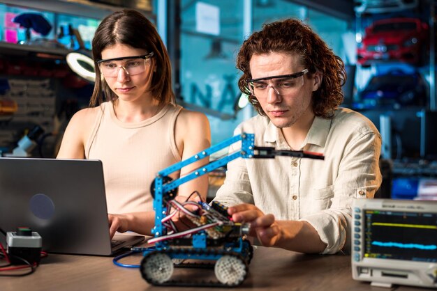 Joven y mujer con gafas protectoras haciendo experimentos de robótica en un laboratorio