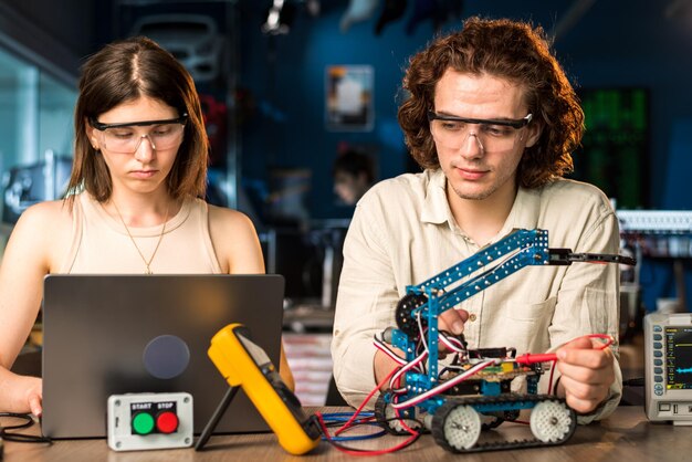 Joven y mujer con gafas protectoras haciendo experimentos de robótica en un laboratorio