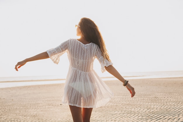 Joven mujer hermosa delgada en la playa al atardecer